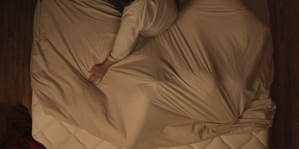 someone laying in the fetal position in bed, with someone sitting next to them.